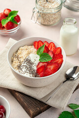 Bowl with oatmeal, fresh strawberries and chia seeds on a soft pink background.