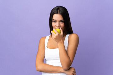 Teenager girl isolated on purple background eating an apple
