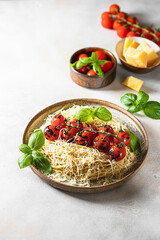 Spaghetti, pasta with a branch of grilled cherry tomatoes with basil and parmesan on a light concrete background.