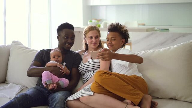 Happy multiethnic family looking at smartphone together on sofa in big house Spbd.