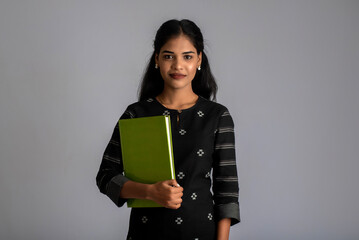 Pretty young girl holding book and posing on grey background