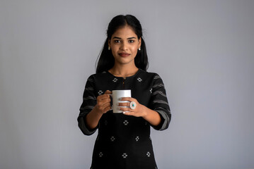 pretty young girl with a cup of tea or coffee posing on grey background