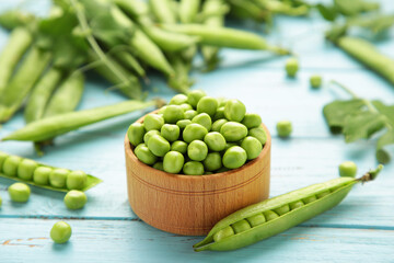 Green peas in wooden bowl on blue wooden background
