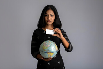 young girl holding the world globe and posing with credit card on a grey background.