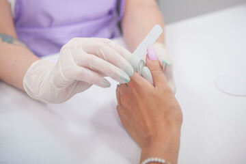 Cropped shot of manicurist filing thumb fingernail of female client