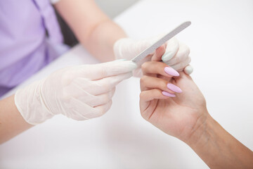 Close up of manicurist using nail filer, working with female client