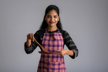 Young girl holding kitchen utensils spatula and pan on a grey background