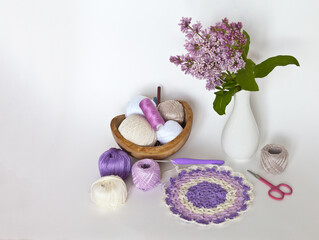 Obraz na płótnie Canvas Spring still life with needlework and crochet. Hand crochet accessories and beautiful hand knitted round lace doily. A sprig of blooming lilacs in a vase on a white background. Empty space for text