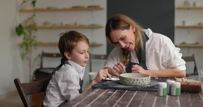Female caucasian potter helping his son making pattern on the clay bowl. Slow motion