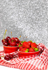 Juicy Fresh Strawberries and Sweet Cherry in a Red Bowls on piece of cloth on a silver sparkling background. Vitamin food