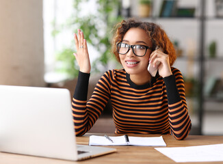 Cheerful young african american woman talking someone on mobile phone while working remotely or studying online from home