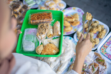 female buyer uses tong tongs to select and take the fried food to the plastic tray before placing the plastic bag