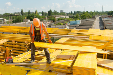 A worker in a safety helmet assembles a formwork from wooden panels - obrazy, fototapety, plakaty