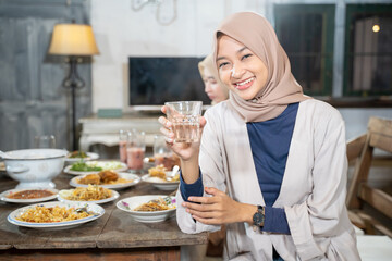 a veiled woman smiles at the camera holding a glass to break the fast together in the dining room