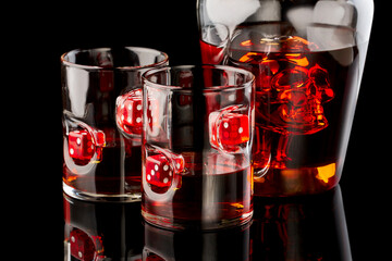 Whiskey glasses with rum or whiskey with red dices and decanter with scull on dark glass background