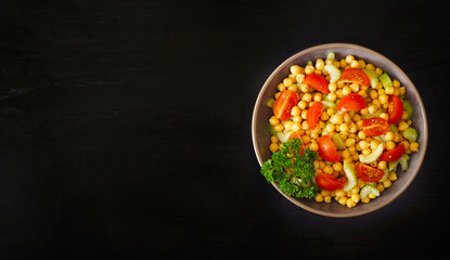 Healthy and vegetarian salad with chickpea, celery and tomato on a dark background.  Top view. Place for text  