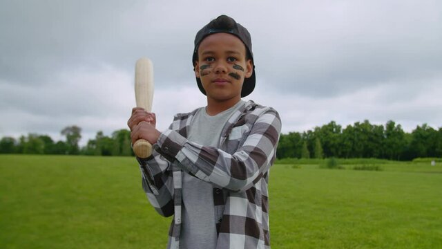 Portrait of serious confident lovely school age boy baseball hitter with baseball bat wearing eye black, ready to hit a shot and waiting for pitch while enjoying playing baseball game on green field.