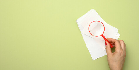 a stack of paper sales receipts and a woman's hand with a red plastic magnifying glass on a green...