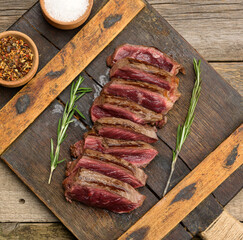 classic beef steak uncooked meat ,fried outside, red inside, with red juice, cut into pieces on a wooden board