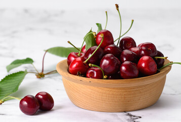 ripe red cherries in a brown wooden plate on a white table