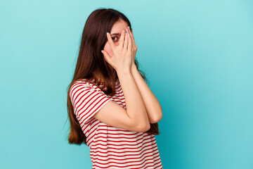 Young caucasian woman isolated on blue background blink through fingers frightened and nervous.