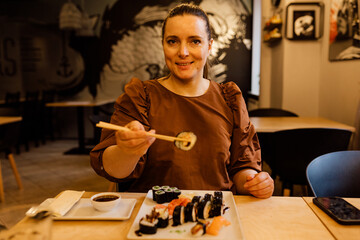 European woman uses chopsticks in a restaurant at a cafe table and looks into the camera. Japanese culture