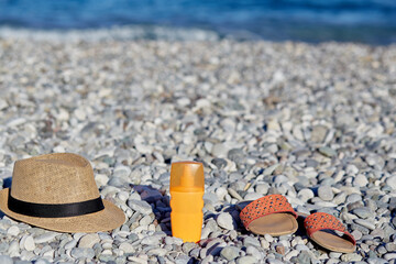 Fototapeta na wymiar Mock up of sun cream, summer slippers and hat on the beach. Concept of spa, beauty, cosmetic, suncream and moisturizer. Summer concept.