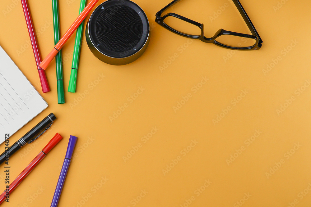 Wall mural View from above of a mini speaker, eyeglasses, and colorful pencils on the yellow background