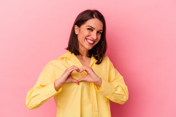 Young caucasian woman isolated on pink background smiling and showing a heart shape with hands.