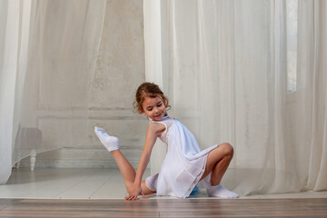 Pretty girl does gymnastics in a dress on the background of a white curtain. children's sports concept.
