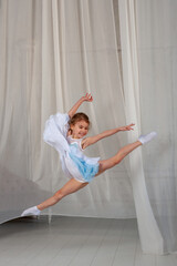 Pretty girl jumping in a dress on the background of a white curtain. children's sports concept.