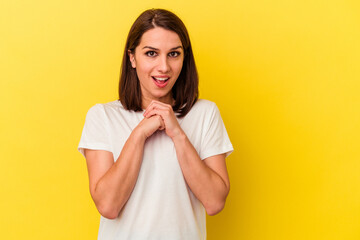 Young caucasian woman isolated on yellow background praying for luck, amazed and opening mouth looking to front.