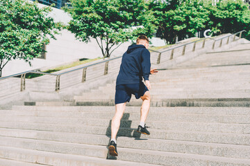 Young athlete man runner running up and down on city stairs in summer on morning run, background...