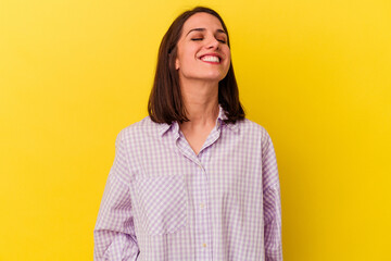 Young caucasian woman isolated on yellow background laughs and closes eyes, feels relaxed and happy.
