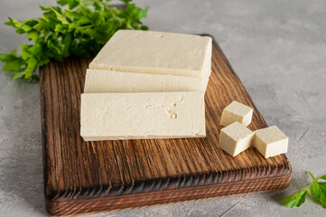 Fresh cheese tofu from soybeans with parsley on a board on a gray concrete background. A vegan product. Copy space.