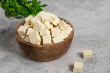 Fresh cheese tofu from soybeans with parsley on a board on a gray concrete background. A vegan product. Copy space.
