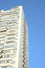 A high-rise building is seen from below during the day against the background of the blue sky. Space for the text