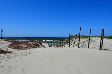 A view of a sandy beach located next to the Baltic Sea with hilltops visible and wooden poles attached to metal fences separating Polish land from the Russian Federation seen on a sunny day 