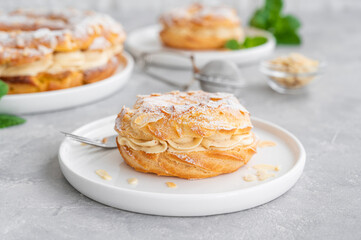 French traditional cake Paris Brest with praline cream, powdered sugar and almond petals on top on a gray concrete background. Copy space.