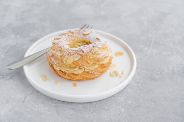 French traditional cake Paris Brest with praline cream, powdered sugar and almond petals on top on a gray concrete background. Copy space.