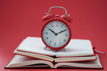 Alarm clock standing on pile of books on red background closeup