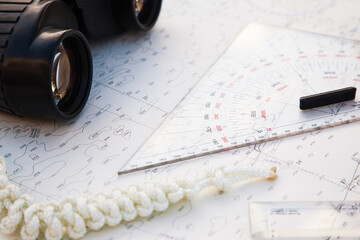 Navigation tools are on the navigation map. Marine ruler, binoculars, and next to it lies a white...