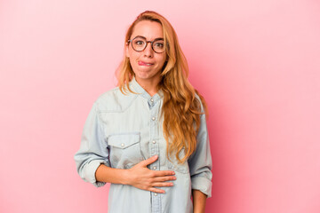 Caucasian blonde woman isolated on pink background touches tummy, smiles gently, eating and satisfaction concept.