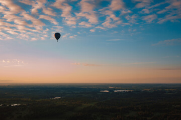 A balloon flying over a forest in a rural area against a background of blue and red sky