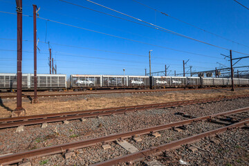 Fototapeta na wymiar Train Locomotives Transporting New Car Vehicles in Cargo Carriers on Rail Track Networks