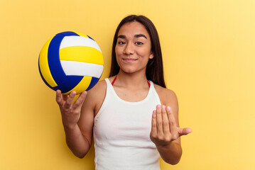 Young mixed race woman playing volleyball on the beach isolated on yellow background pointing with finger at you as if inviting come closer.