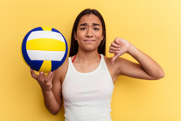 Young mixed race woman playing volleyball on the beach isolated on yellow background showing a dislike gesture, thumbs down. Disagreement concept.