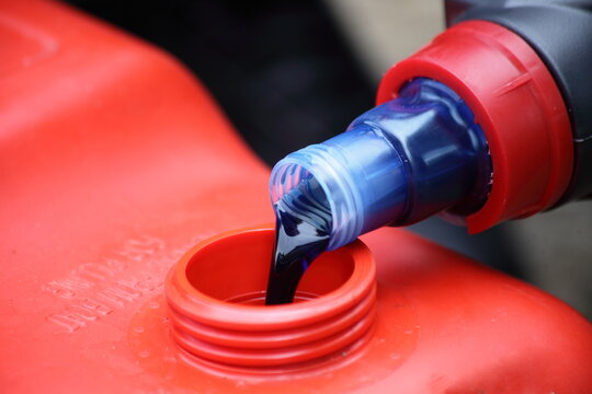 Premixing of a fuel mixture of gasoline and 2T blue motor oil for a two-stroke outboard motor in a red plastic boat gas tank closeup
