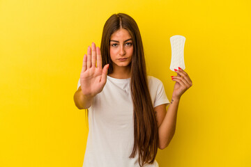 Young caucasian woman holding a compress isolated on yellow background standing with outstretched hand showing stop sign, preventing you.