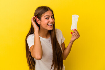 Young caucasian woman holding a compress isolated on yellow background trying to listening a gossip.